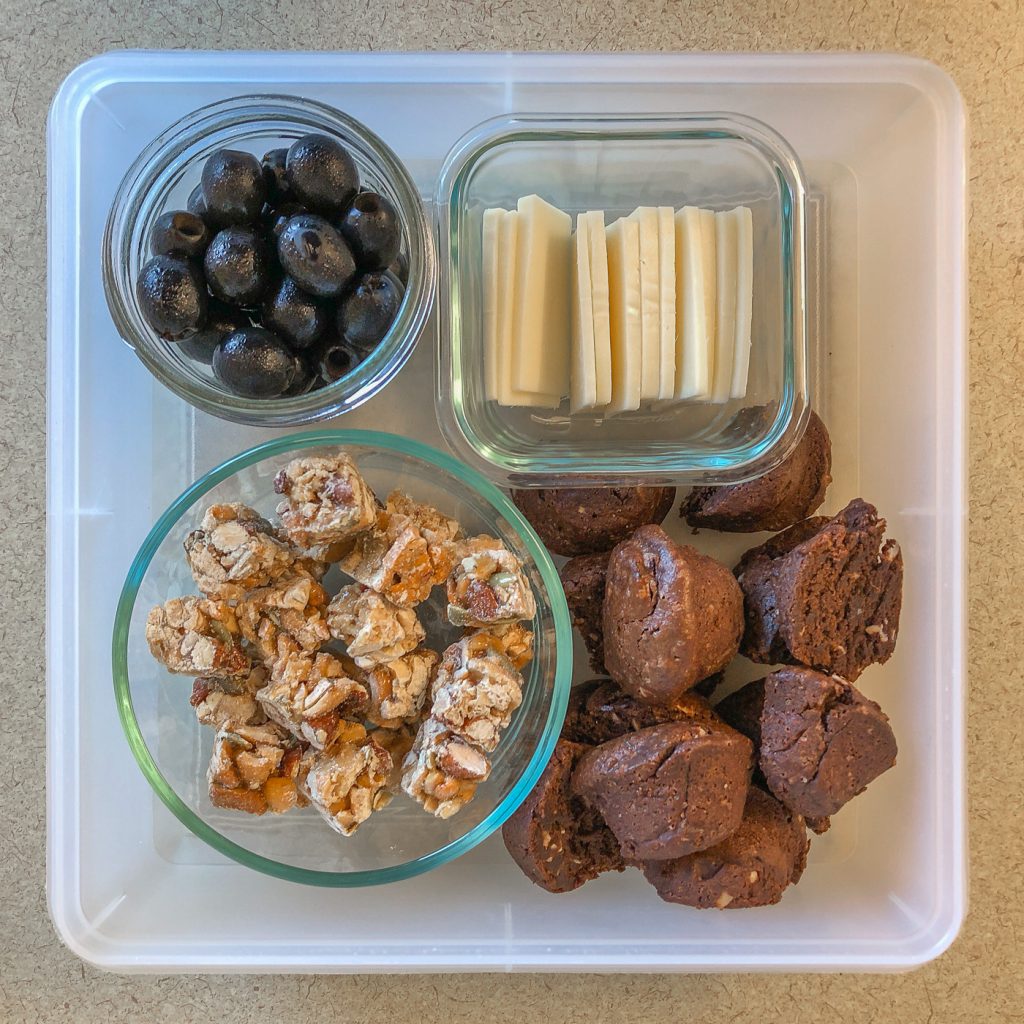 Plastic container with nut clusters, olives, cheese, and brownie bites